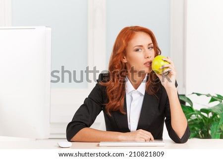 Young businesswoman eating apple at work. closeup of red-haired girl sitting at office desk