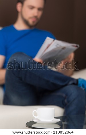 Man sitting on sofa relaxed and reading. guy reading magazine, wearing casual clothes.