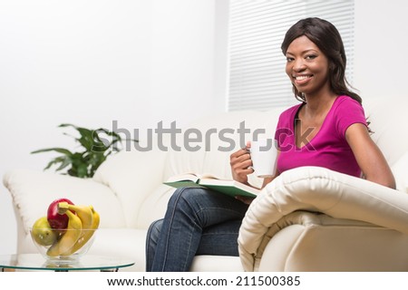 profile of relaxed young woman reading book. beautiful girl sitting on sofa at home indoor and smiling