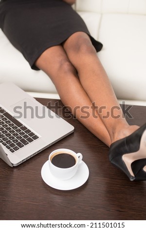 legs of young black girl with laptop computer. Woman sitting in bright living room on sofa with feet on table