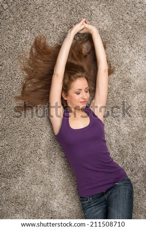 Relaxed woman lying on floor indoors and smiling. Beautiful young woman lying on floor