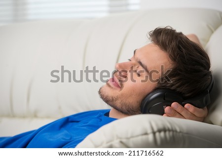 Man enjoying music lying on couch. Dreaming man listening to music at home