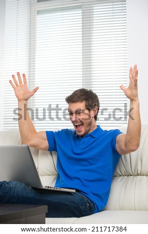 Young man happy on sofa with laptop. handsome male in t-shirt sitting on sofa at home and smiling.