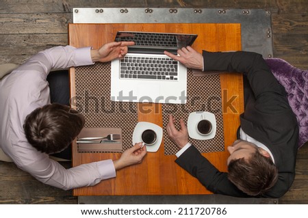 two businessmen sitting in cafe and looking at screen. top view of two colleagues met in restaurant drinking coffee
