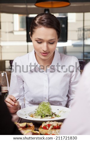 Young woman eating mixed vegetable salad in cafe. Woman eating healthy salad lunch in cafe with friends