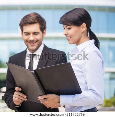 Businessman looking at paperwork with businesswoman. Businessman and woman looking at black folder