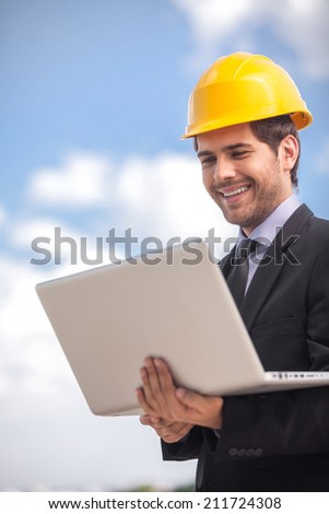 handsome architect man holding laptop. Young man in business suit against blue background