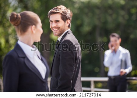 Three happy business partner people talking outside. brunette girl looking at man and smiling outside