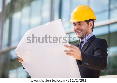Architect in yellow hardhat holding plan. young construction reviewer wearing workwear
