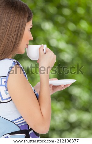Happy beautiful woman with coffee cup in hands. profile of brunette drinking coffee in park outside