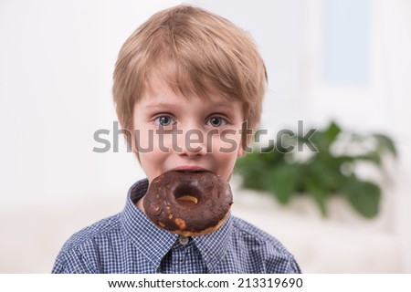 closeup of blonde boy eating doughnuts. portrait of cute little boy biting sweets