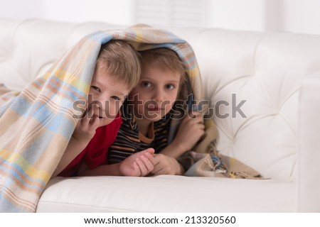 Two children looking into camera under blanket. two friends hiding under coverlet and smiling