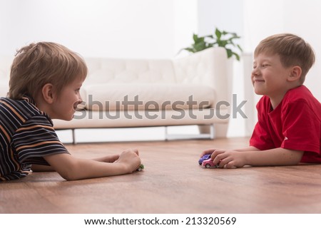 Two friends playing on floor at home. side view of boys playing with toy cars and smiling