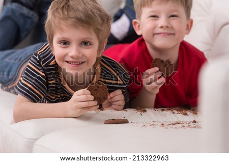 two cute boys lying on couch. two friends eating cookies and smiling