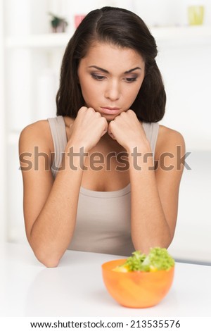 upset young woman keeping diet and eating vegetables. Sad woman in front of her small diet meal