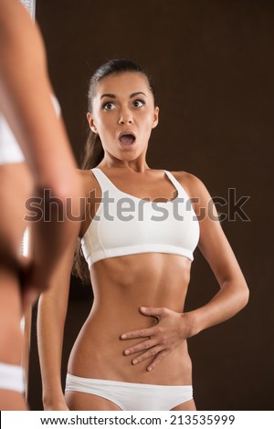 scared young woman looking into mirror. beautiful girl standing without clothing in surprise