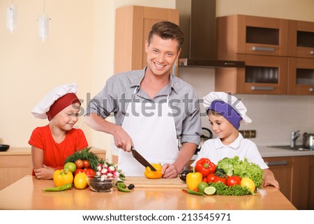 Young father teaching children how to prepare salad. boy and girl learning to cook food at kitchen