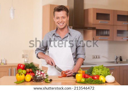 handsome man cutting pepper on chopping board. guy preparing food at kitchen counter