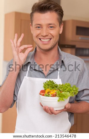 handsome man holding bowl of fresh salad. guy preparing tasty food at kitchen