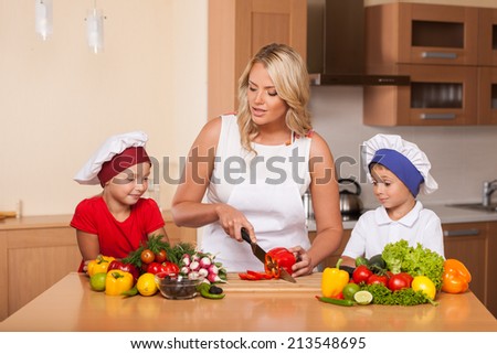 Young mother teaching children how to prepare salad. boy and girl learning to cook food at kitchen