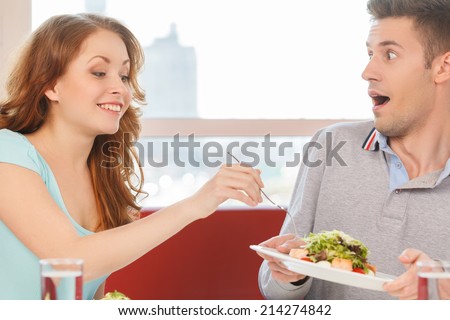 woman holding fork and eating man\'s salad. man holding plate with salad and moving away