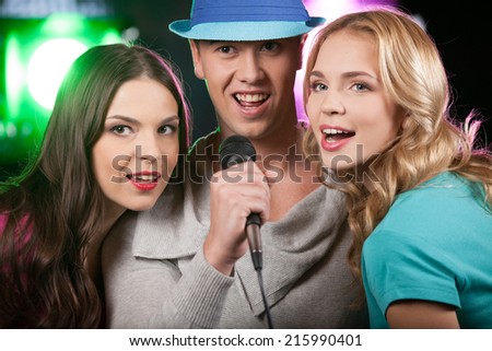 Group of three friends singing with microphone. closeup of man with blue hat standing on black background and singing