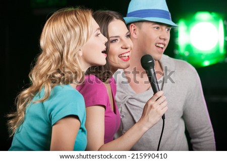 Group of three friends singing with microphone. profile of man and women standing on black background and singing