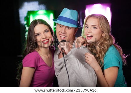 Group of three friends singing with microphone. man with blue hat standing on black background and singing