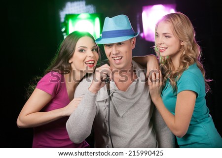Group of three friends singing with microphone. man and two women standing on black background and singing