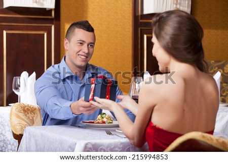 Smiling attractive man giving woman present. While drinking wine at lunch break