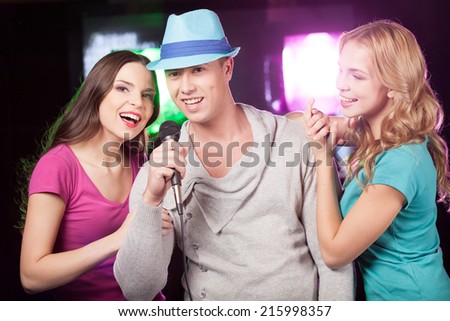 Attractive women and man singing karaoke. beautiful trio standing at bar and singing in mic