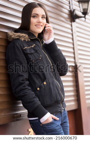 Beautiful woman talking on cell phone. brunette woman standing near wall and smiling
