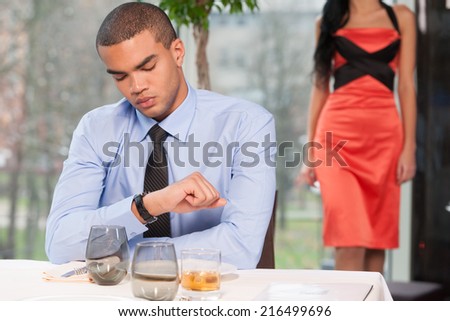 Handsome man waiting woman and looking at watch. woman walking behind late to date