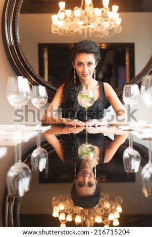 pretty young woman drinking in restaurant. closeup of girl sitting at table with mirror behind