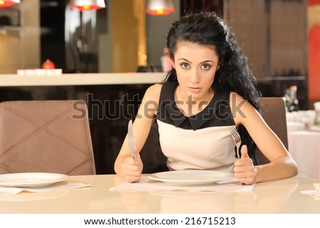 hungry young woman waiting for food. pretty girl sitting at table with knife and fork