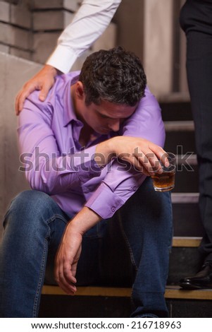 Handsome young man talking to drunk man sitting on stairs. closeup of guy drinking whisky and sleeping