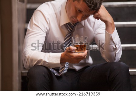 Handsome young man sitting on stairs. closeup of guy drinking whisky and thinking