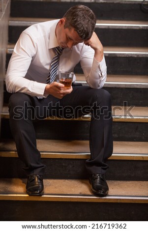 Handsome young man sitting on stairs. portrait of guy drinking whisky and thinking