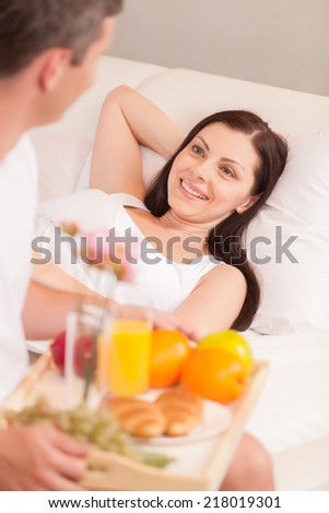 young man bringing breakfast in bed. beautiful brunette lying in bed and smiling