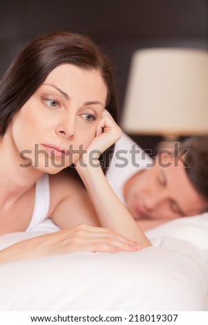 closeup of unhappy woman lying in bed stressed. couple having problem while man sleeping