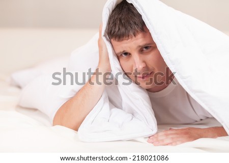 sad man hiding in bed under sheets. image with young caucasian male model home in bed.