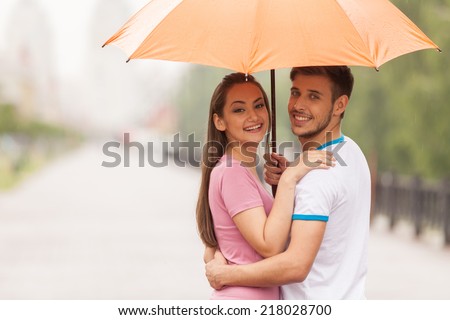 couple under umbrella standing turned around. man huging woman and holding unmbrella