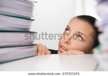 Business woman sitting under table and looking on folders. beautiful girl hiding under table from work
