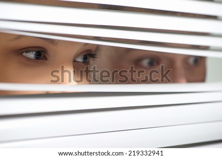 Young Couple observing through jalousie. young woman peeking through closed blinds or shutters.