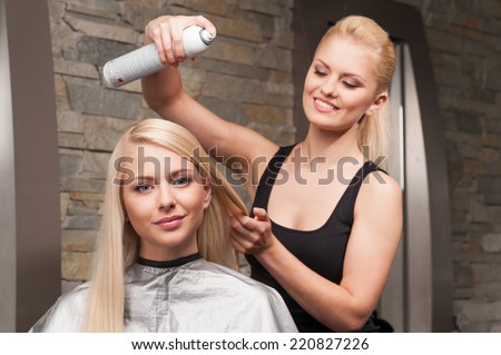 blond hairdresser applying spray on client\'s hair. Female hairdresser works on woman hair in salon