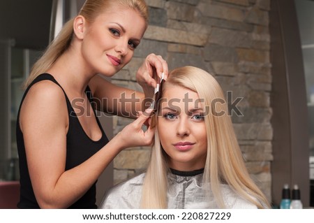Blond girl selecting tone of hair in hair salon. Female client and blond hairdresser choosing shades of colour in salon