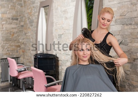 Stylist drying hair of female client at beauty salon. Young female beautician giving new hair style to woman at parlor