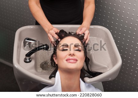 Smiling woman having her hair washed at hairdresser's. Hairdresser washing hair of woman in barber shop.