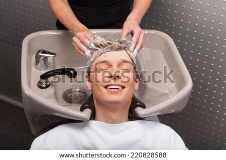 Close-up of young smiling caucasian man having his hair washed. Portrait of happy client with closed eyes at salon