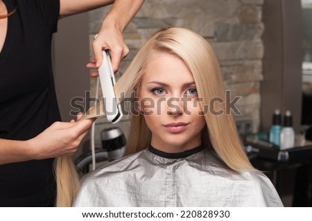 closeup on young woman getting new haircut by hairdresser at parlor. hairdresser straightening client's hair in beauty salon